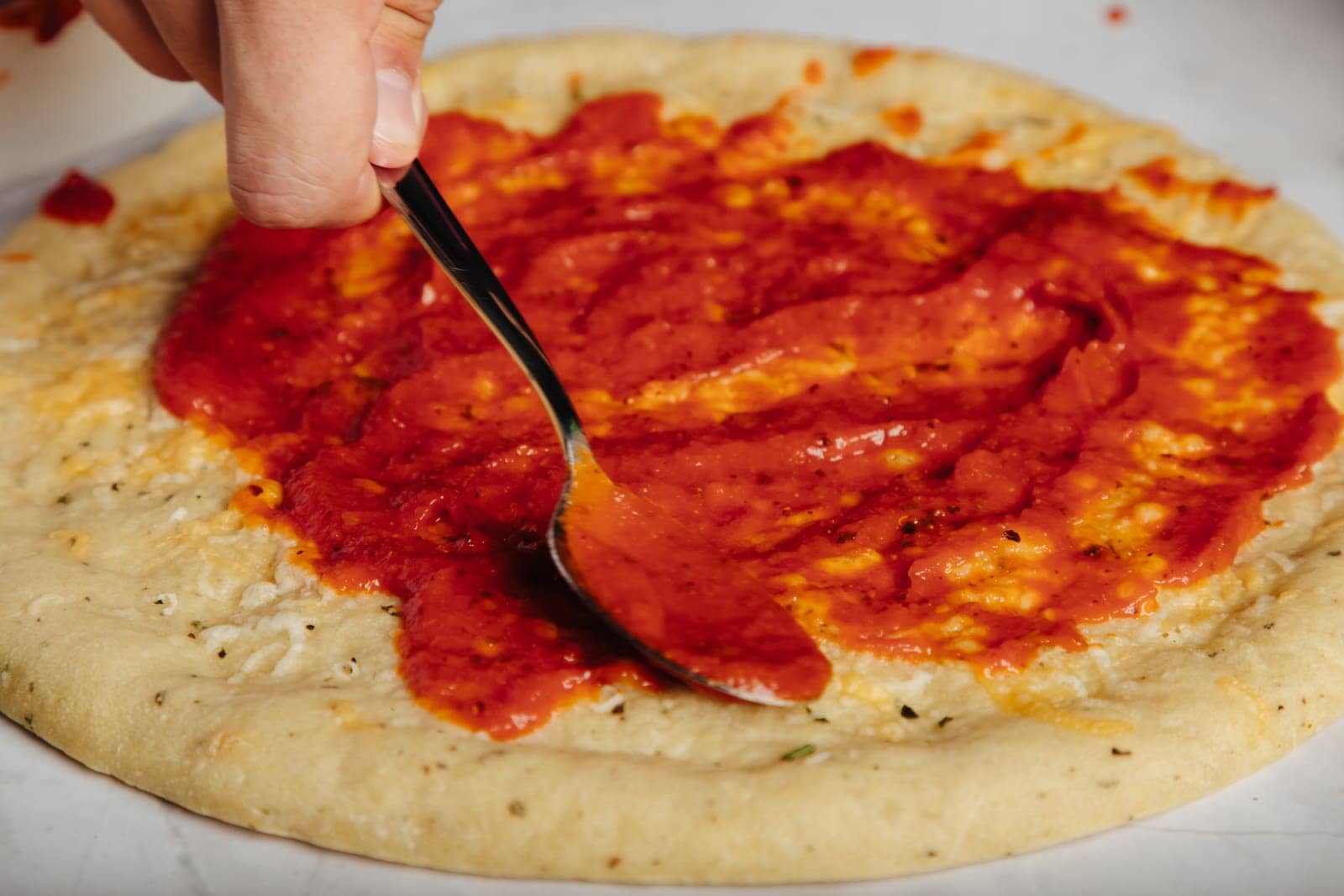 Spreading sauce on a handmade Bee-Transformed pizza crust